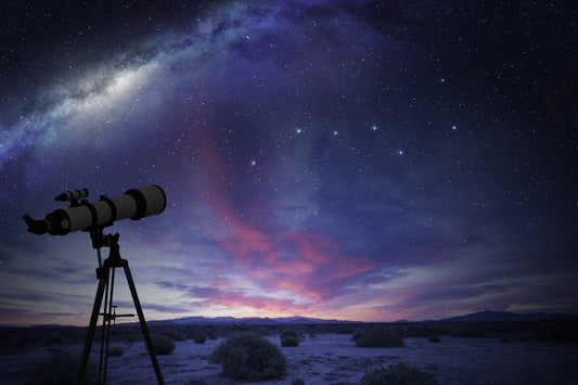 A white telescope set up on a snowy landscape looking up at the stars just after sunset with dark pink and purple clouds in the distance.